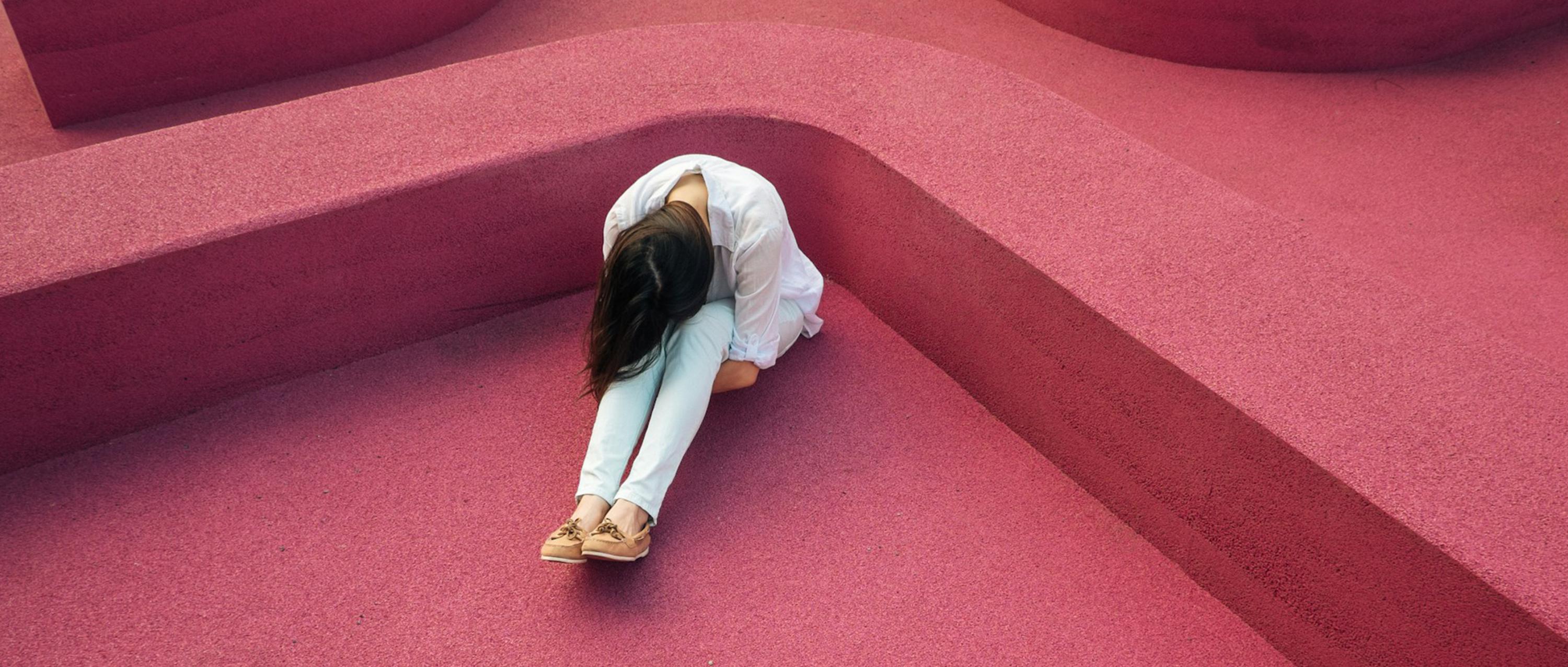 Women sitting on the floor looking down with her arms wrapped around her legs.