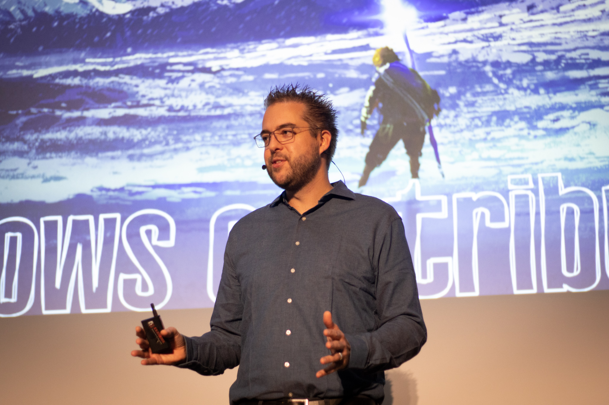 Dries Buytaert onstage standing in front of a large screen at DrupalCon Prague. His hands are outstretched and he is speaking to an audience