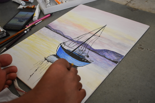 Painting in real time of a sailboat in a body of water. Painter using foot to hold brush.