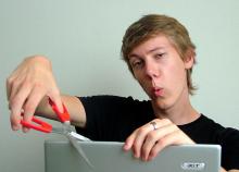 White man holding scissors as if about to cut a laptop lid. 